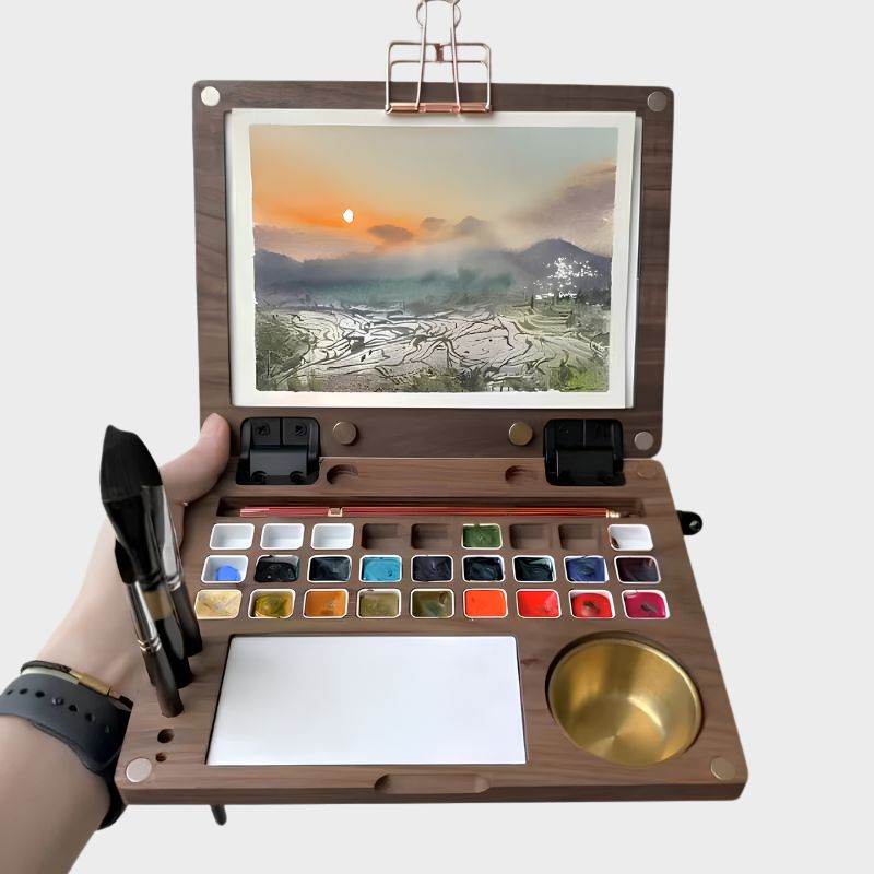 Hand holding the open ArtMate Master Edition walnut watercolor box, a finished sunset rice-terraces painting clipped to the lid above the 27-pan palette, mixing tile and brass water pot