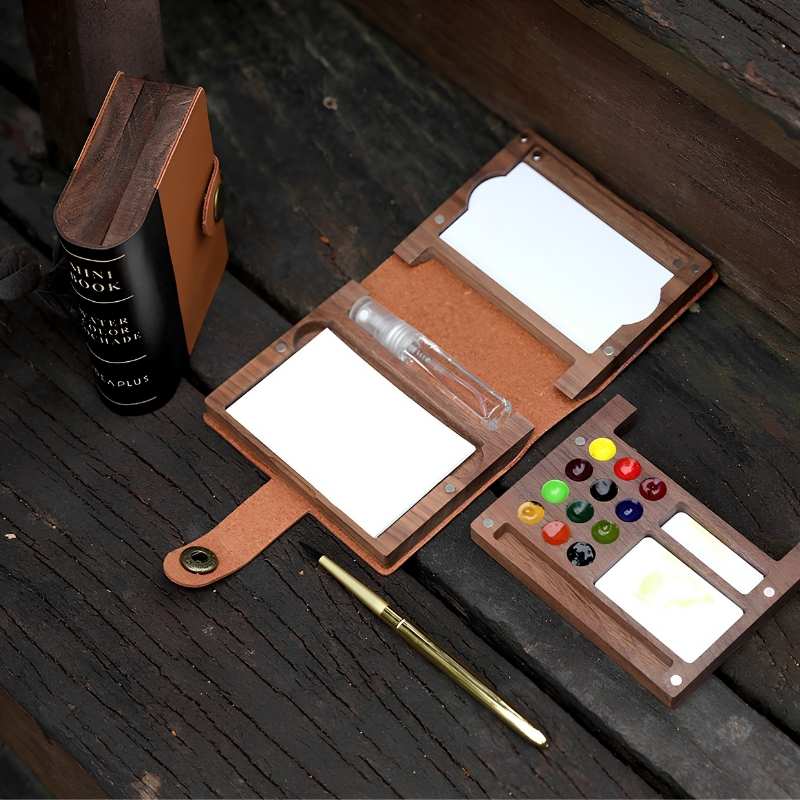 Walnut folio kit open on a wood deck beside its book-style case, with brush, water vial and 12 paints