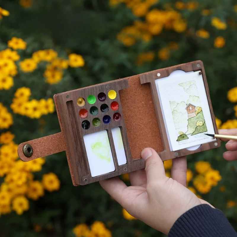 Open walnut folio art kit with 12 paints and a landscape painting in a field of yellow flowers
